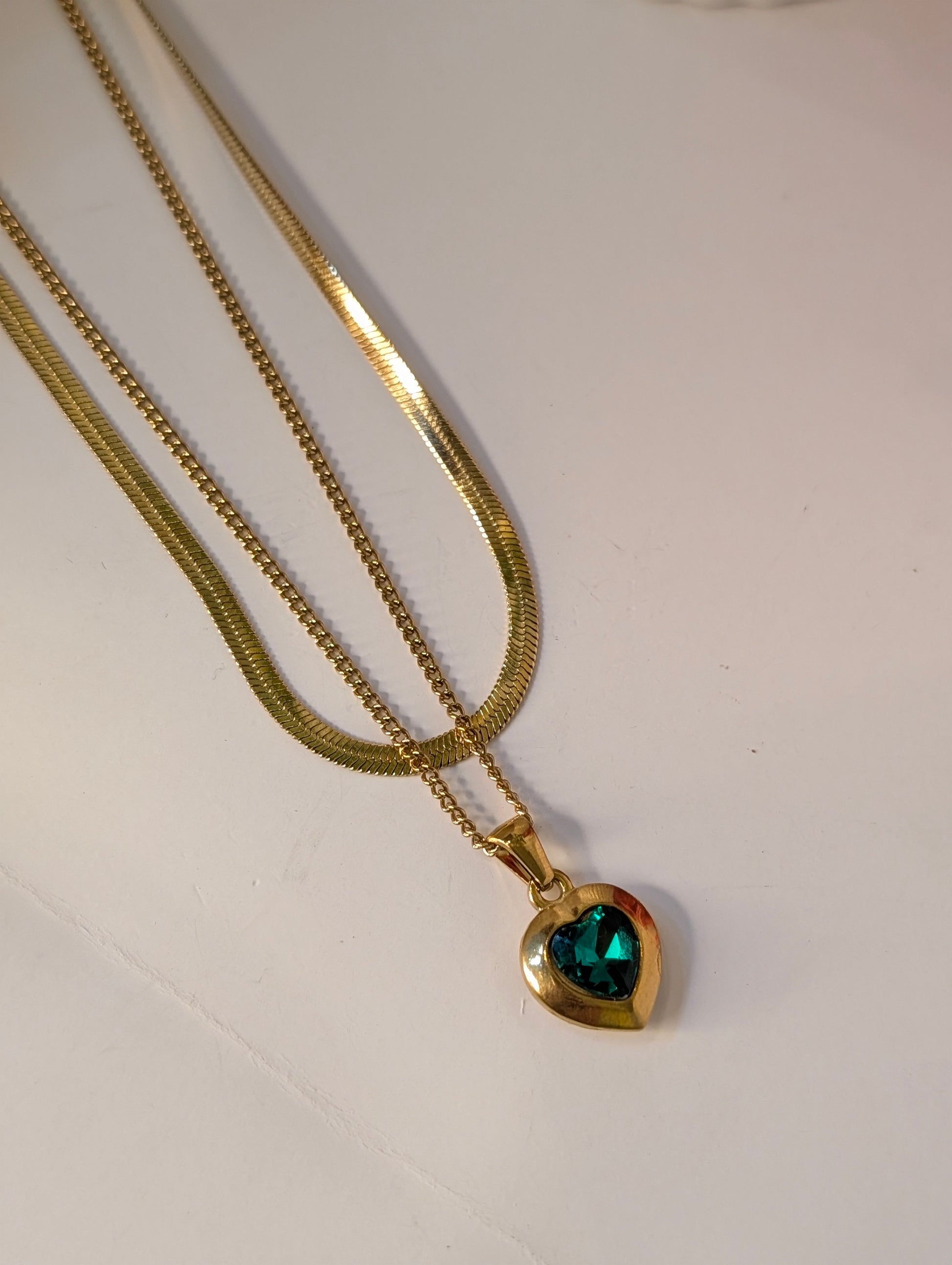 Gold necklace with a green heart-shaped pendant on a white background