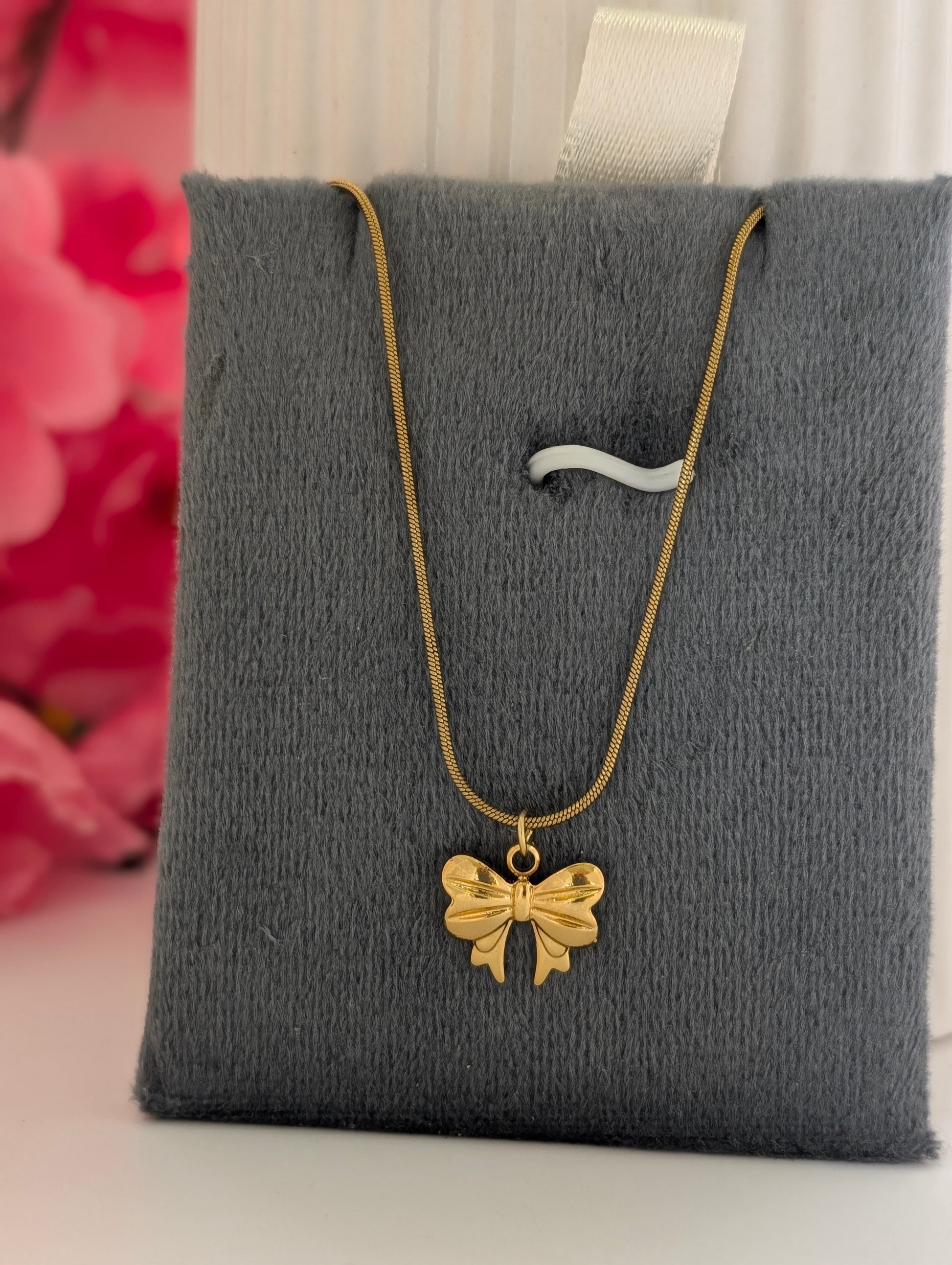 Gold necklace with a bow pendant on a gray jewelry pillow.