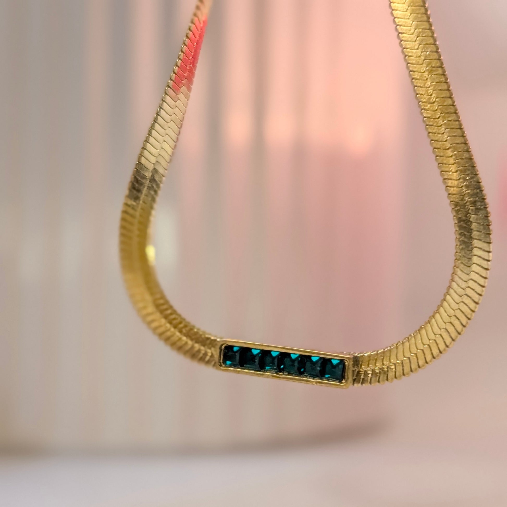 Gold necklace with blue stones on a soft pink background