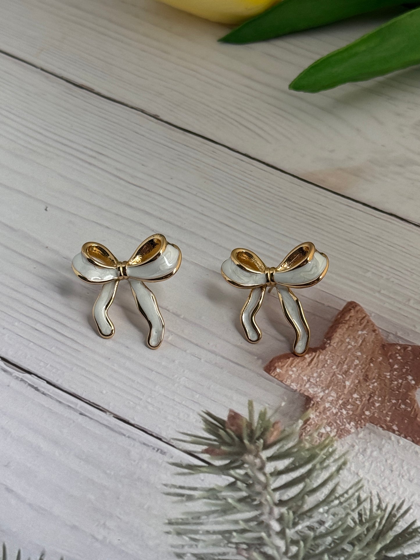 Gold bow-shaped earrings on a wooden surface with decorative elements.
