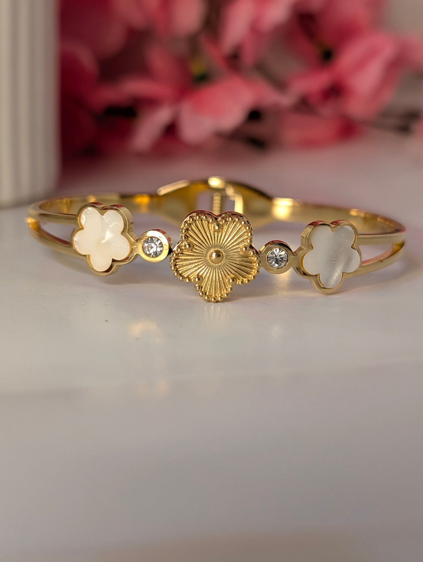 Gold bracelet with floral designs on a white surface with pink flowers in the background