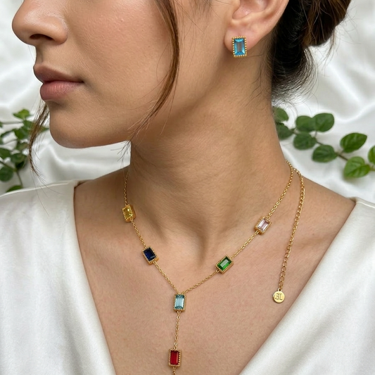 Close-up of a woman wearing a gold necklace with colorful gemstones and matching earrings.