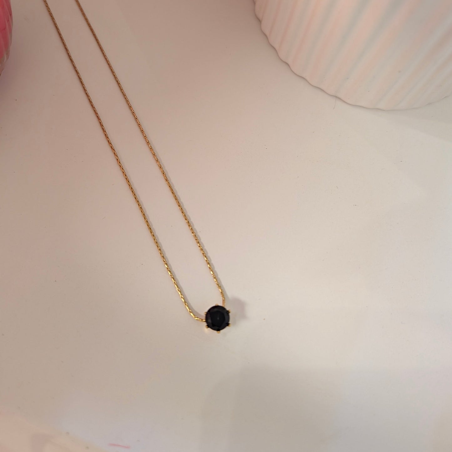 Gold necklace with a black pendant on a light surface