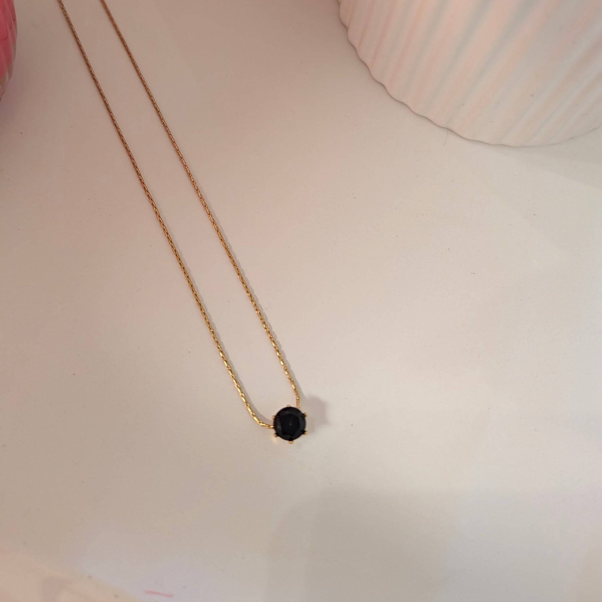 Gold necklace with a black pendant on a light surface