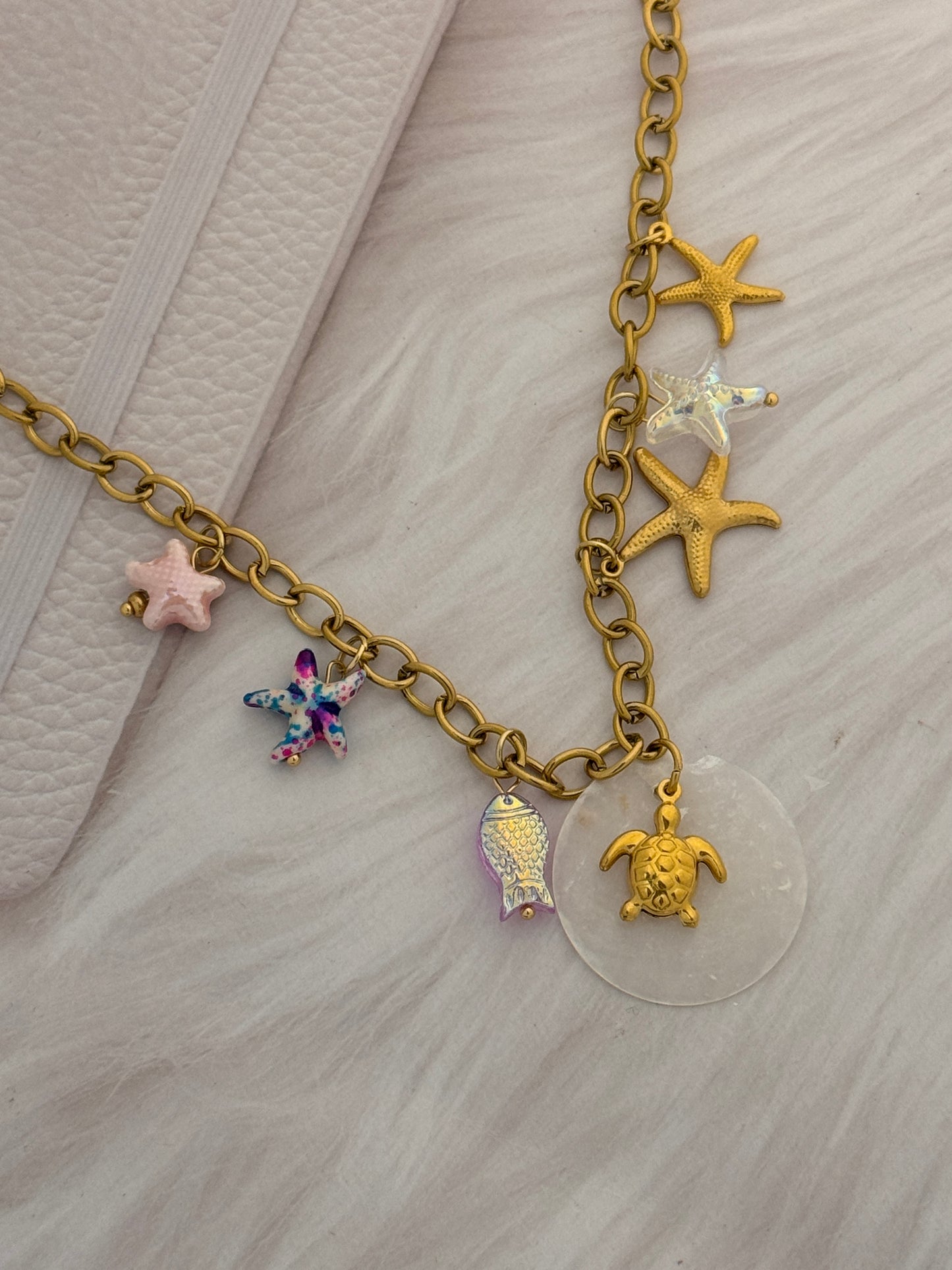 Gold chain bracelet with various charms on a light gray background