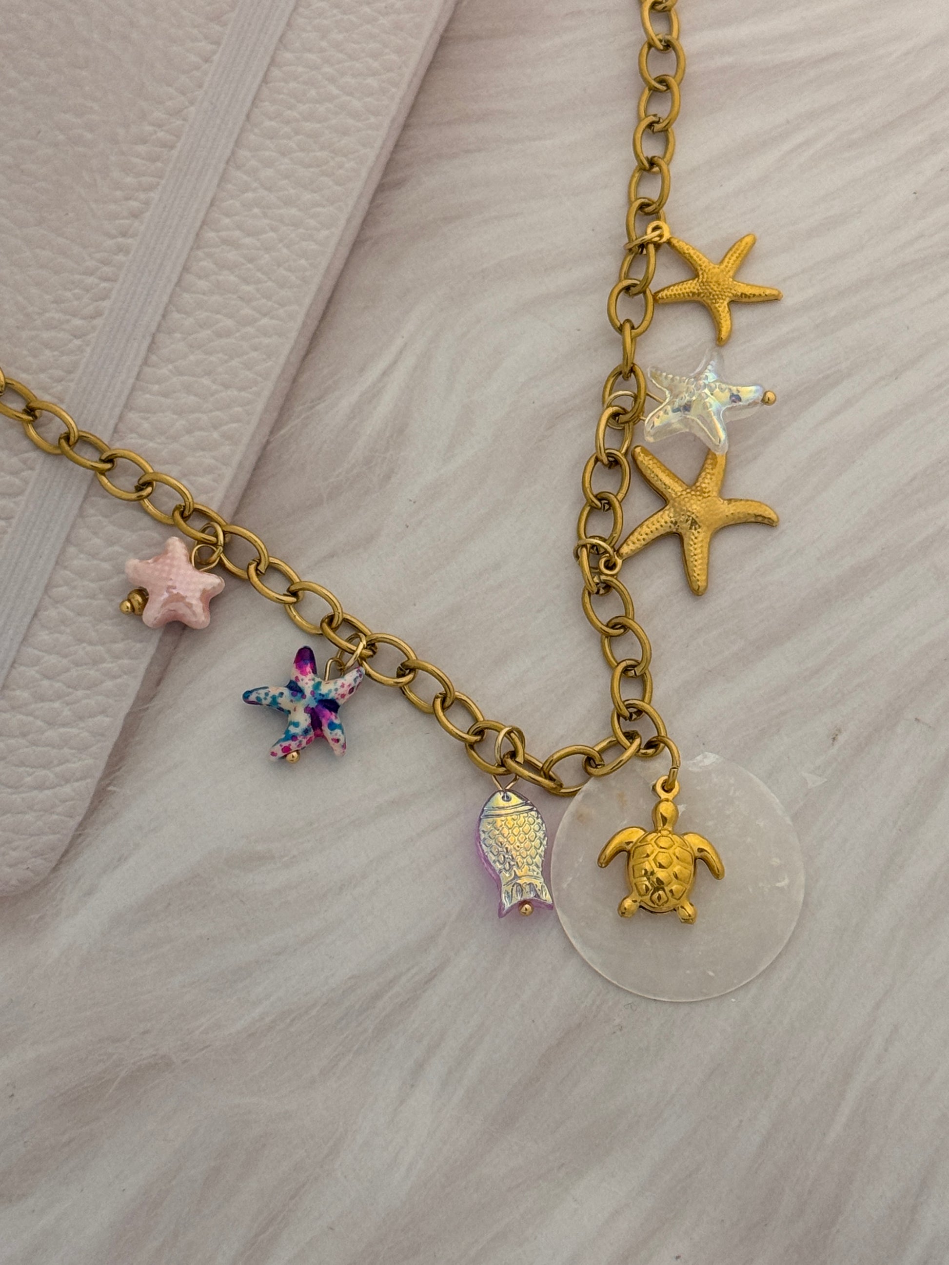 Gold chain bracelet with various charms on a light gray background