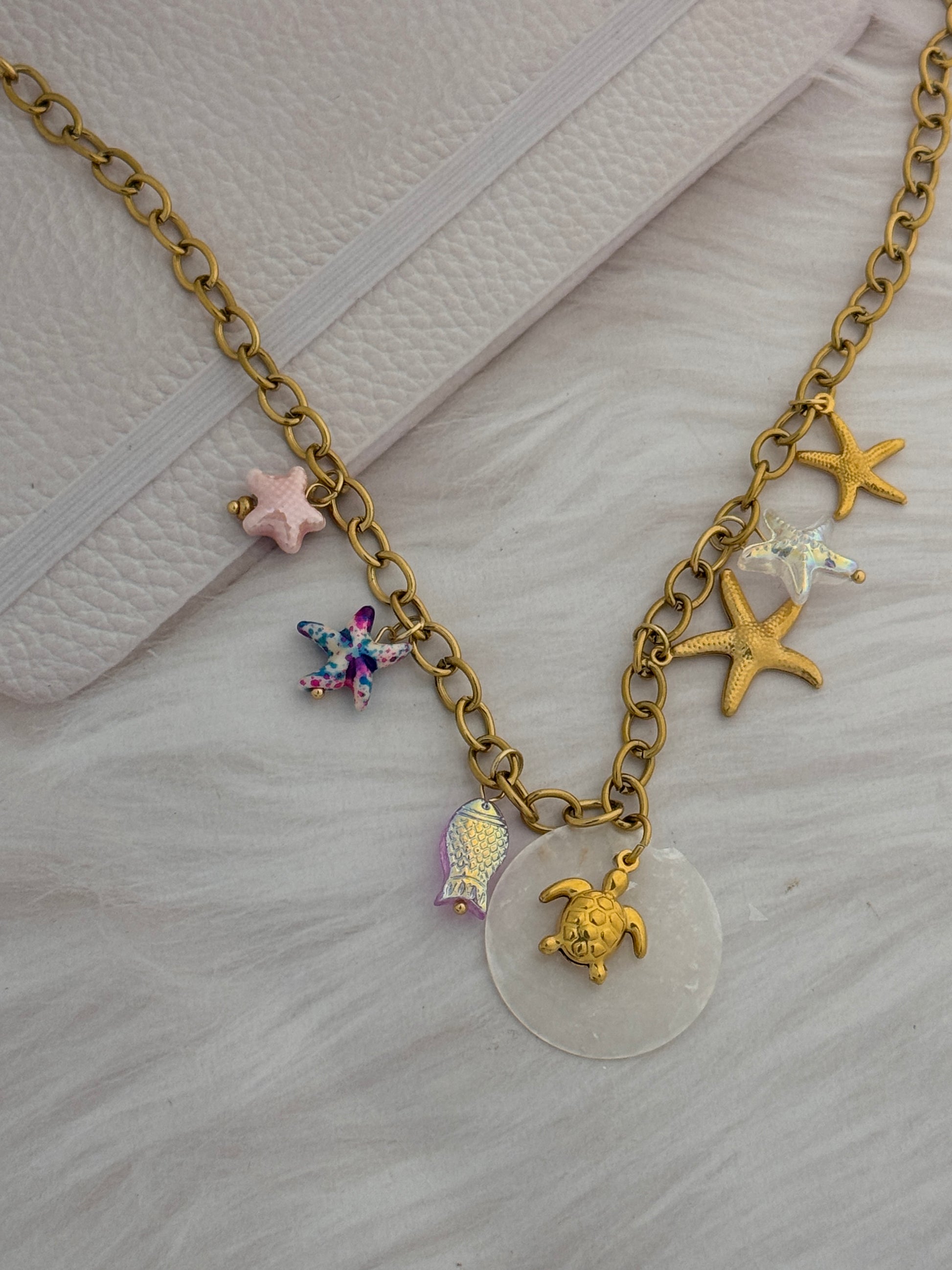 Gold chain bracelet with various charms on a light gray surface