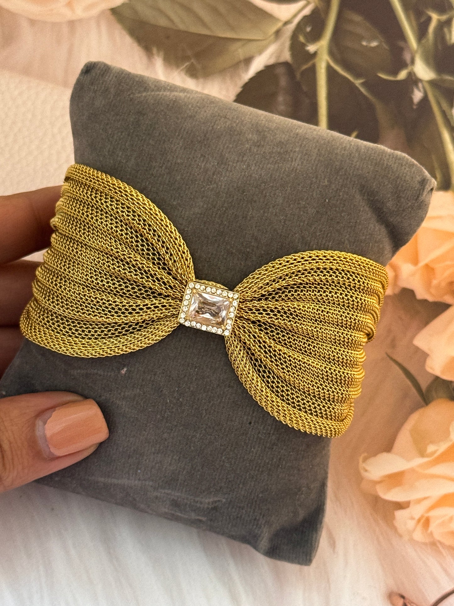 Gold mesh bow with a diamond-like center on a gray pillow.
