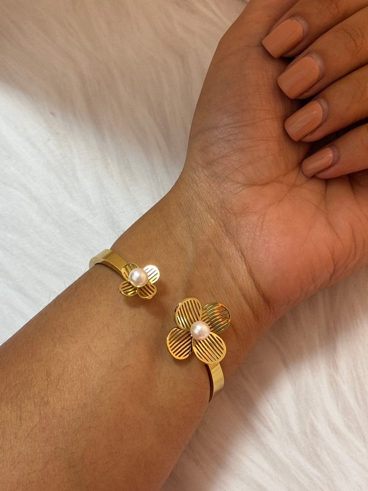 Gold bracelet with floral design on a wrist against a neutral background
