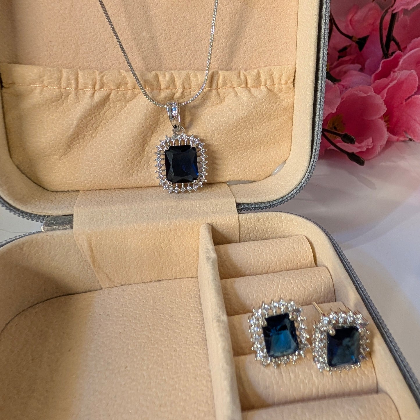 Jewelry set with necklace and earrings in a beige jewelry box with pink flowers in the background.