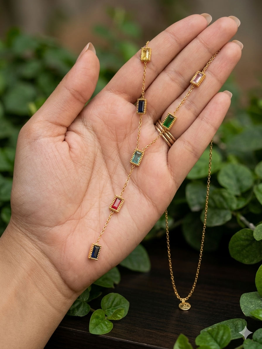 Gold necklace with gemstone pendants held in a hand against a green leafy background