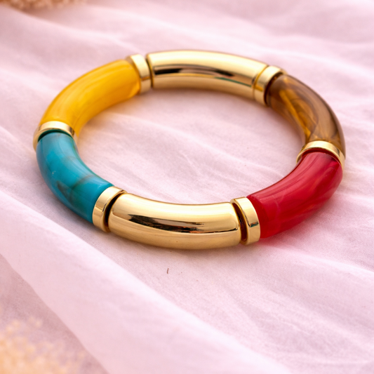 Multicolored bracelet with gold accents on a pink fabric background