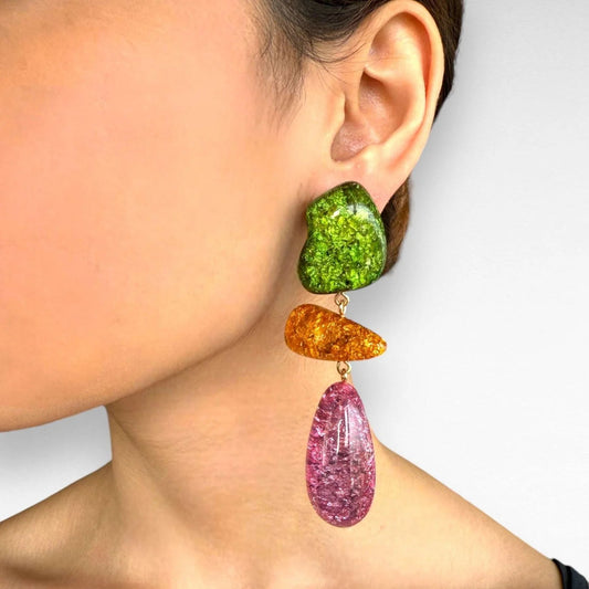 Close-up of colorful earrings worn by a person on a plain background