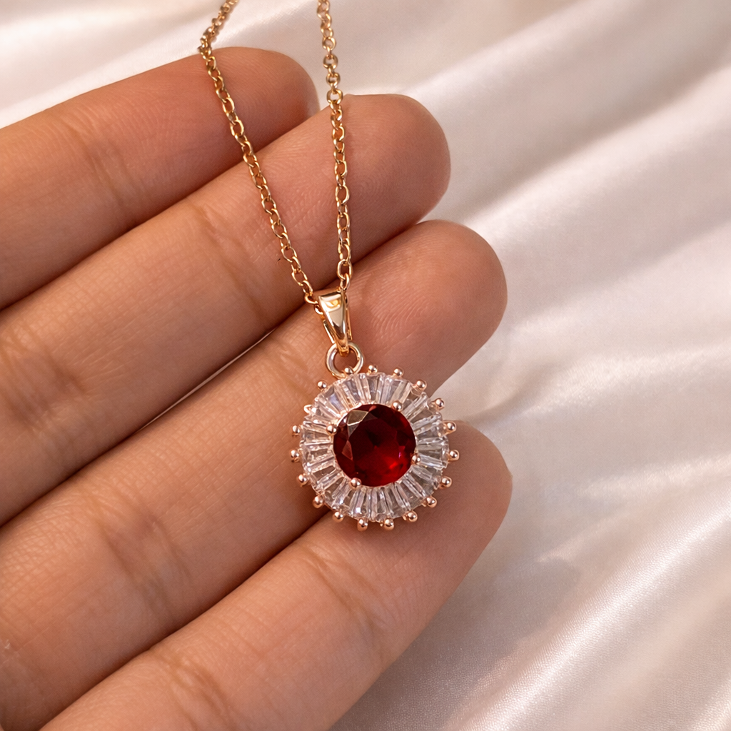 Gold necklace with a red gemstone held between fingers on a light background