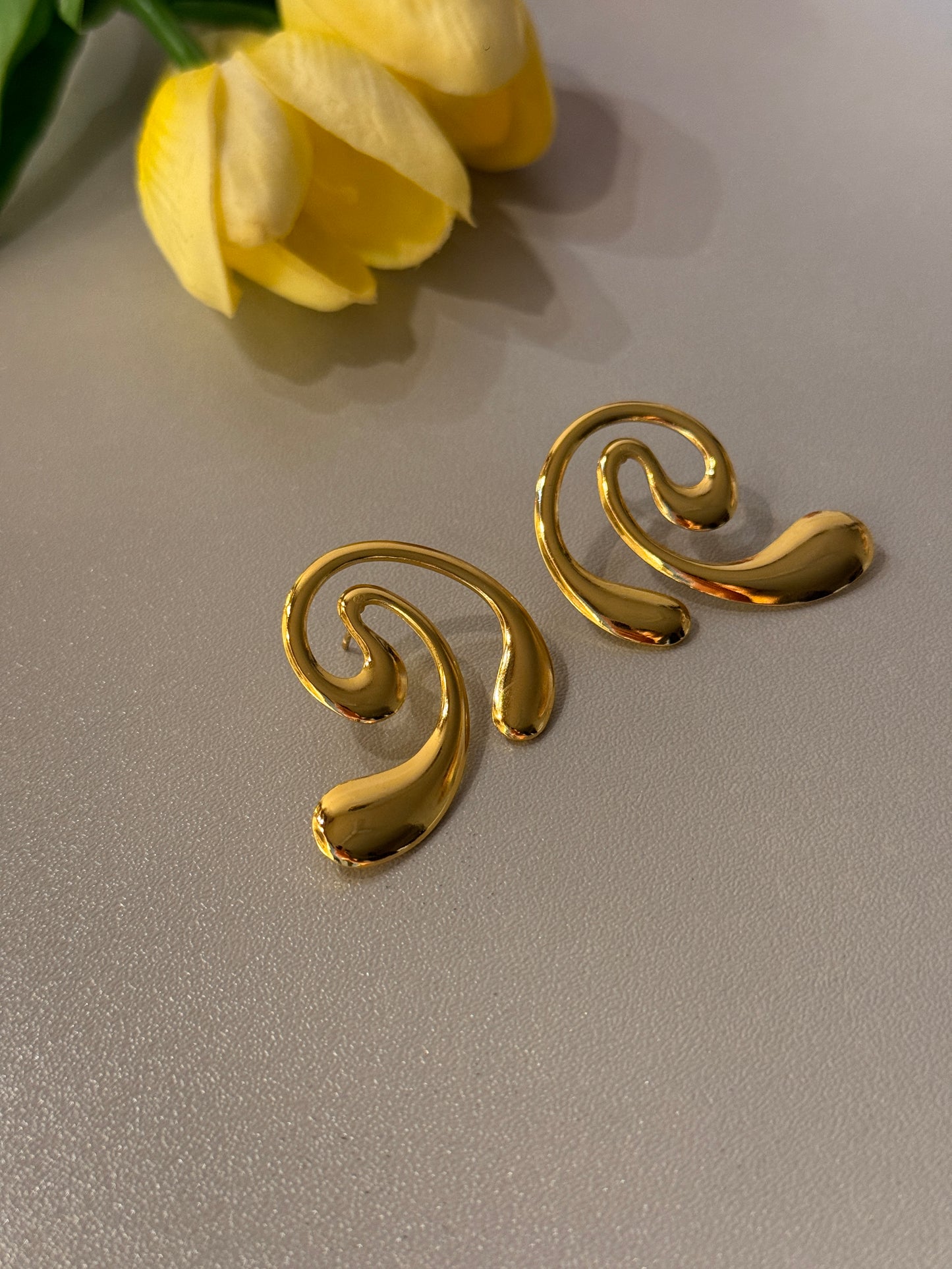 Gold spiral earrings on a light gray background with a yellow tulip.