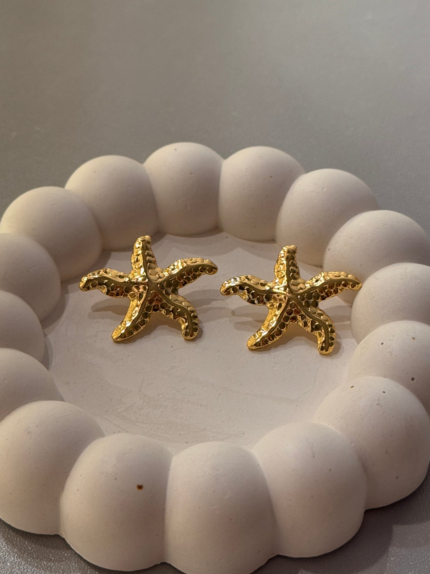 Gold starfish earrings on a white beaded background