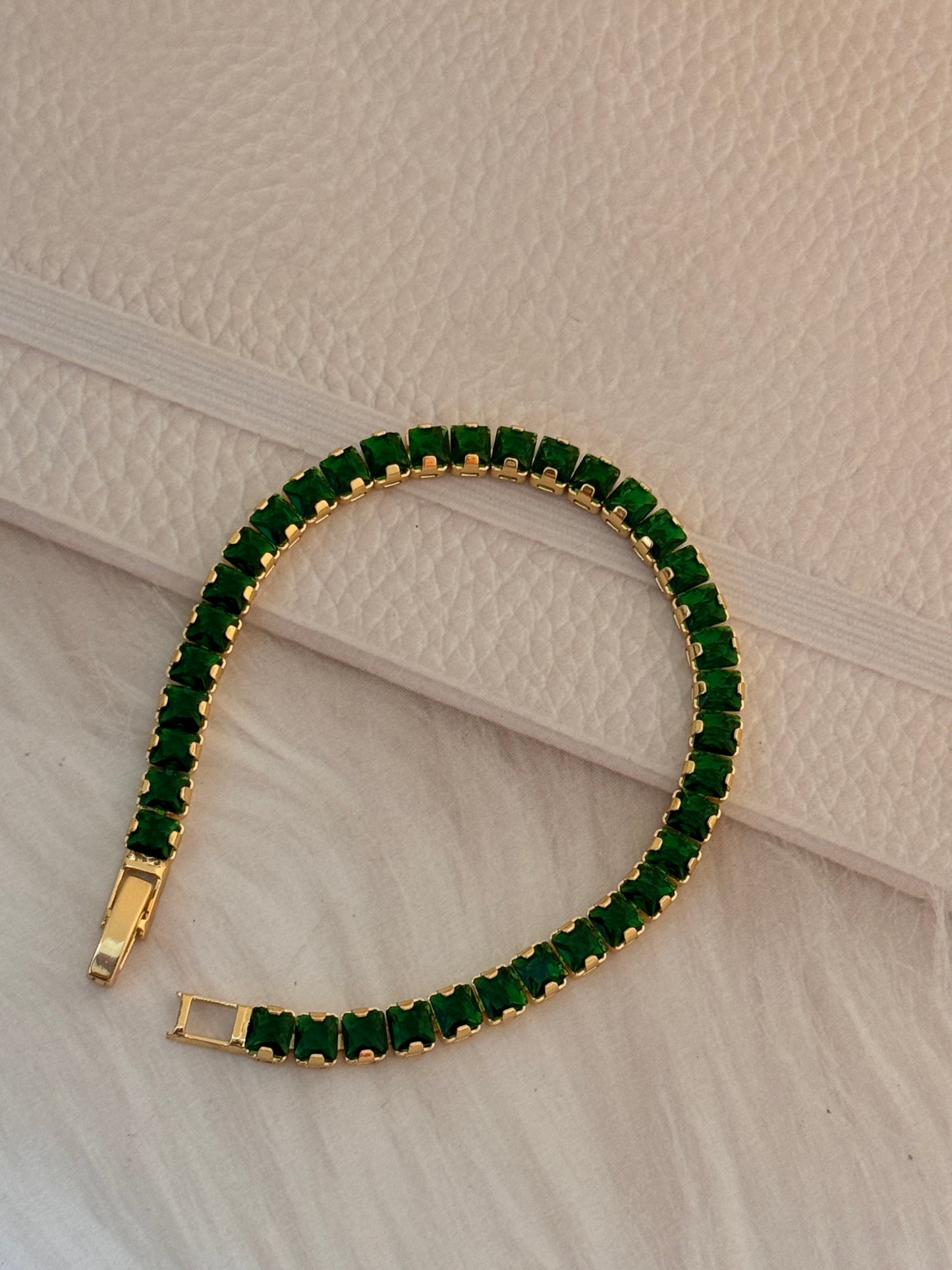 Gold bracelet with green gemstones on a textured beige surface