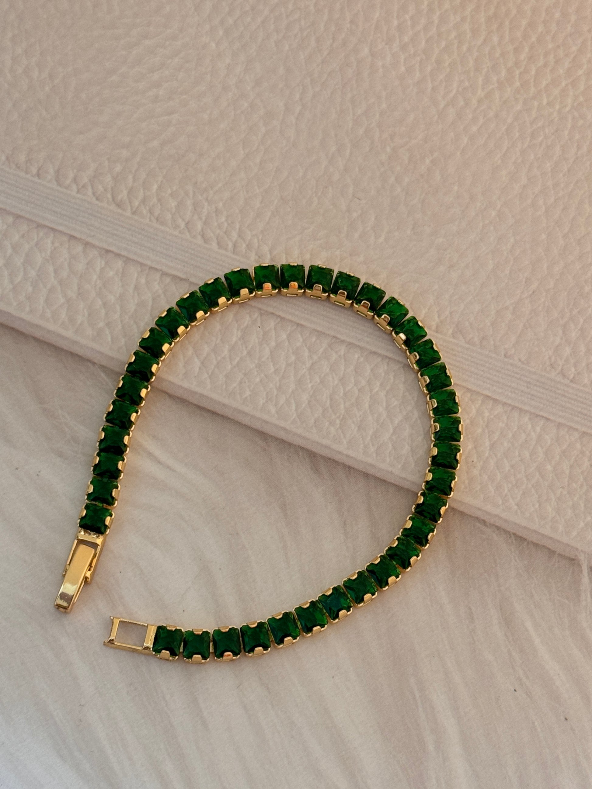 Gold bracelet with green gemstones on a textured beige surface