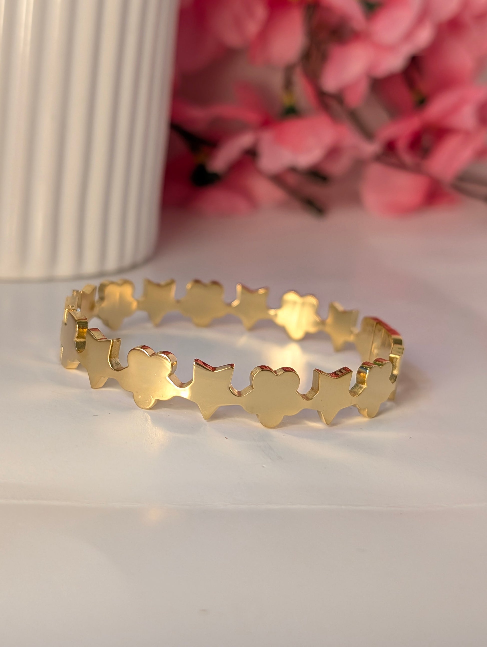 Gold bracelet with star patterns on a white surface with pink flowers in the background