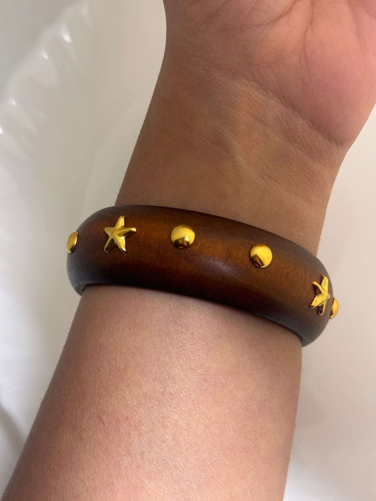 Brown leather bracelet with gold star accents on a wrist against a white background