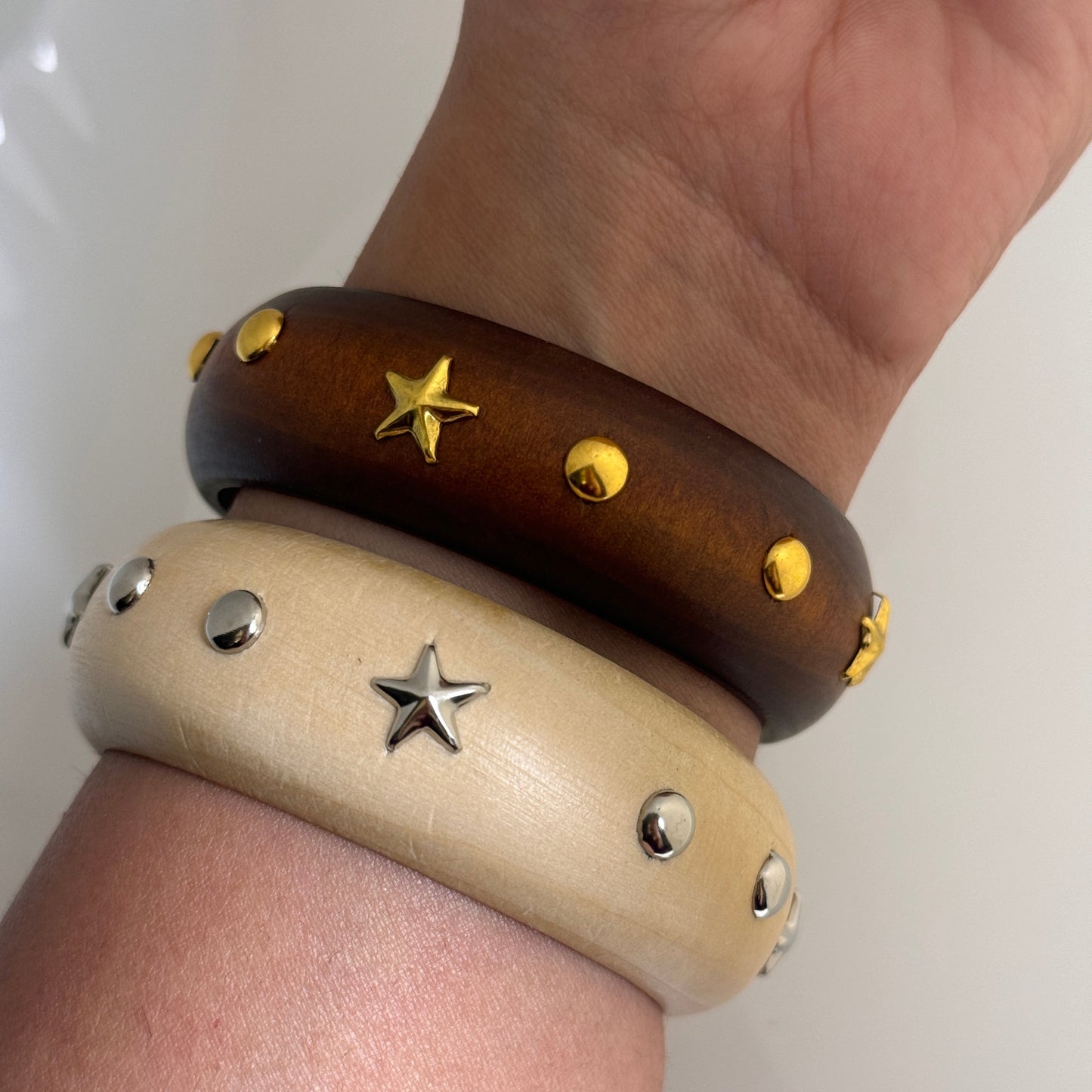 Two bracelets with star and circle studs on a wrist against a white background